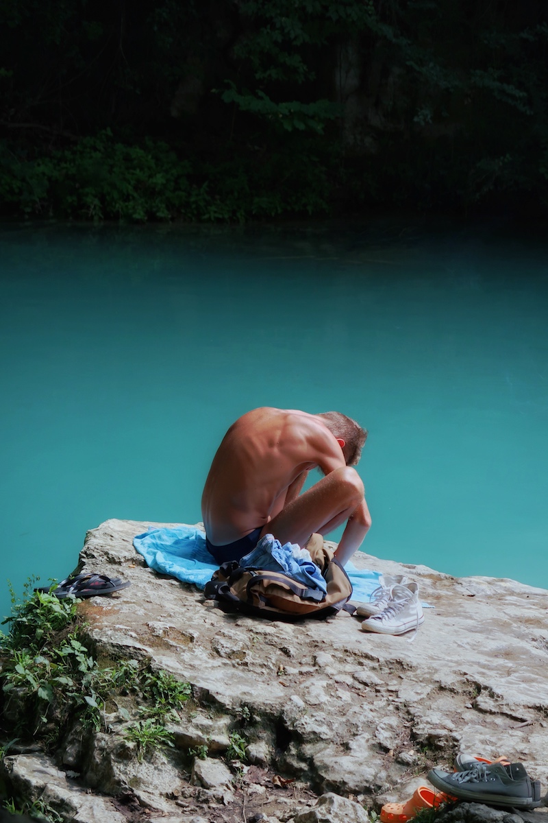 Photograph of shirtless person sitting on their towel  hunched over next to a teal blue river. Second photograph is of Ben Clement (tenant) running in a half-marathon. Third photograph is a self portrait of Ben Clement wearing sunglasses with tree shadows over his face.